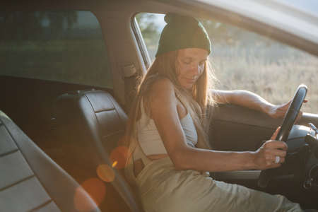 Tired woman in a watch cap napping in the car, leaning on window frame. Eyes closed.の写真素材