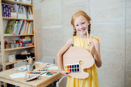 Smiling ginger girl posing for a photo with palette and brushesの写真素材