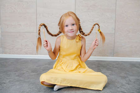 Cute ginger girl sitting on the floor, lifting her braids with brushes