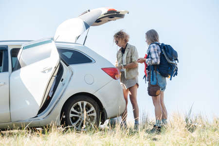 Friends prepare gear for a hike, taking needed stuff from a car trunk. Side viewの写真素材