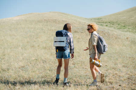 Talking women friends hiking in grassy hills, standing, arguing about somethingの写真素材