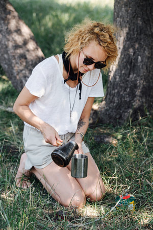Fair-haired woman sitting in a shadow, pouring herself coffee from cezveの写真素材