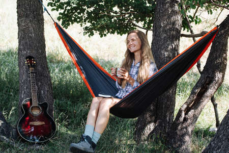 Joyful woman in sunglasses sitting in a hammock, slugging in a shadow, between two big trees....