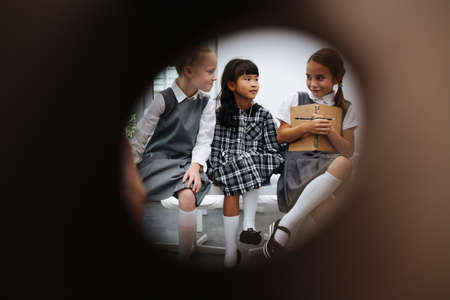 Peeking through a keyhole at three schoolgirls sitting on a desk, gossiping. Black edges.の写真素材