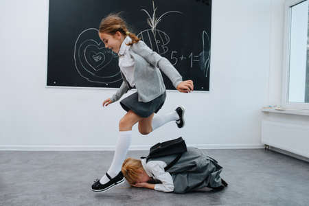 Schoolgirls playing. One is jumping over the other curled up on the floor. Blackboard with drawings in the backgound.の写真素材