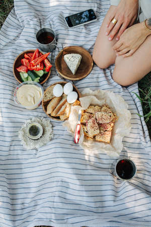 Picnic meal on a blanket. Top view. Girl sitting on her legs in a corner. No face. Tea, eggs, bread,...