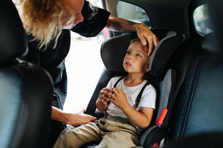 Caring mom giving a head stroke, comforting her little son, sitting on a back seat in a car. From...