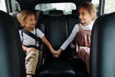 Two loving siblings sitting on a back seat of a car, holding hands, looking at each other. Showing support.の写真素材
