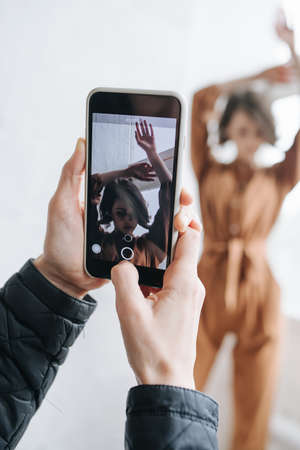Male hands taking photo of a model with smartphone. Selective focus on screen with sensual brunette. Real one is blurred.の写真素材