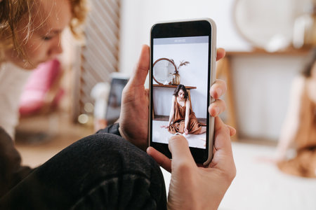 Man taking photo of a model with his smartphone. Crew woman in background. Sensual brunette on the...
