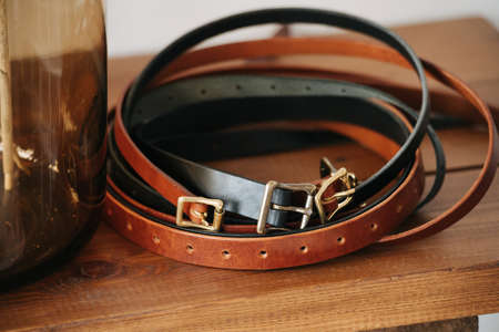 Several waist belts curled up in a circle on a table deck. Next to a glass jar.の写真素材