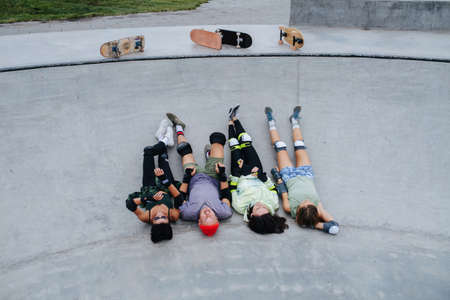 Four skaters chilling on a quarter pipe legs up at skatepark. Wearing some protective gear. Boards lying on the deck. High angle view.の写真素材