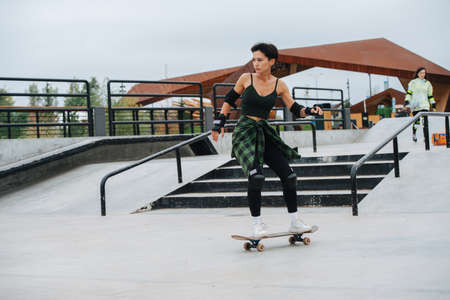Dinamic image of a confident woman skater with short hair riding on her board on concrete paving at skatepark. She wears some protective gear.の写真素材