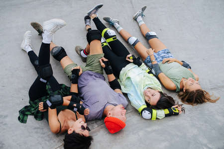 Funny four skaters chilling on a quarter pipe legs up at skatepark. Wearing some protective gear. Talking to each other.の写真素材