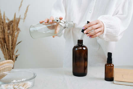 Faceless image of a female chemist preparing a mix for eco friendly cosmetics on a table. Adding liquid in a common brown plastic bottle with a pipetteの写真素材
