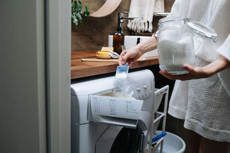 Side view no head image of a woman pouring eco powder in a washer from a big glass jar.の写真素材