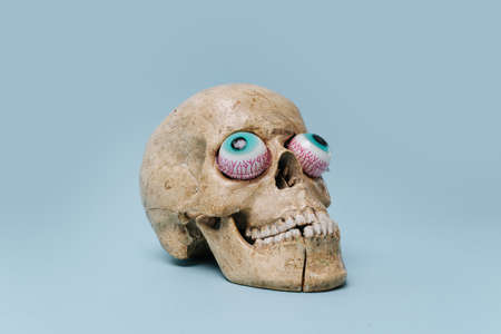 Scull with crooked toy eyes facing outside. Halloween theme. Over blue background.の写真素材