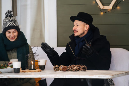 Passionate man telling his story to his friends sitting on a snowy terrace, drinking coffee. Gesturing, woman laughing next to him.の写真素材