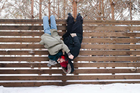 Silly couple kissing while hanging upside down, catching themselves by legs on a wooden fenceの写真素材