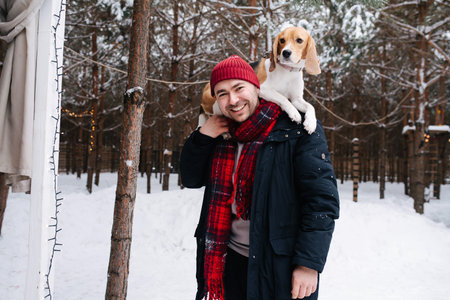 Radiant man playing with a dog, she's lying on his shoulders, she's calmly looking at a distance, taking advantage of her newfound position. Outside in a conifer forest at winter.の写真素材