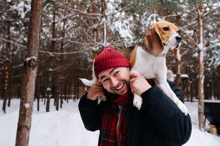 Smiling man playing with a dog, she's lying on his shoulders, she's calmly looking at a distance. Outside in a conifer forest at winter.の写真素材