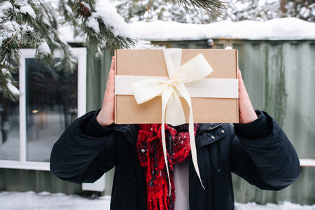 No head image of a man in winter clothes hiding behind the box. Standing in front of a small snowy house.の写真素材