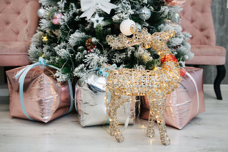 Garland lit deer in front of decorated artificial christmas tree with whitened ends. Bow tied fake presents under it.の写真素材