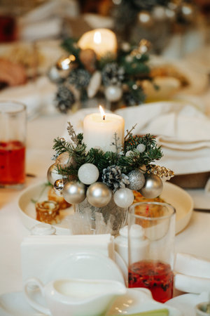 Decorated candle, wrapped with a conifer branch and christmas balls on a dining table. Close up. Blurred background.の写真素材