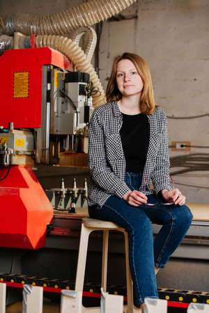 Young woman in semi official clothes sitting on a stool next to a big red piece of heavy machineryの写真素材