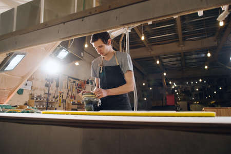Low angle image of a craftsman grinding a wooden plank. In a big spacious workshop.の写真素材