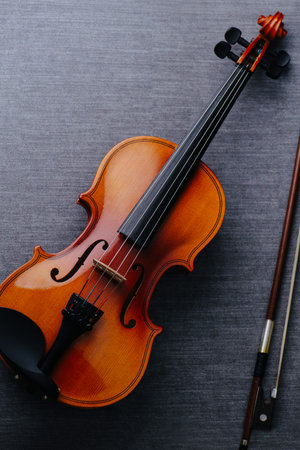 A violin on a gray textile surface. It's in a perfect condition. Next to a bow.