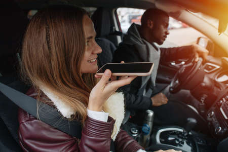Two people in the car. She is talking on a loud speaker, he is driving. Front window is sunlit.の写真素材