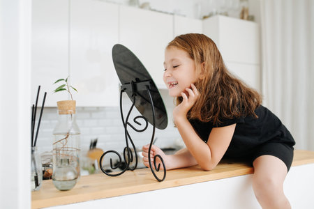 Looking at the mirror little girl checking her missing teeth. Lening close to it. Sitting on a high kitchen table.の写真素材