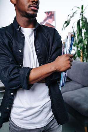 Half face portrait of a stylish black artist, holding bundle of brushes. He is wearing a dark blue dress shirt over a white T shirt.の写真素材