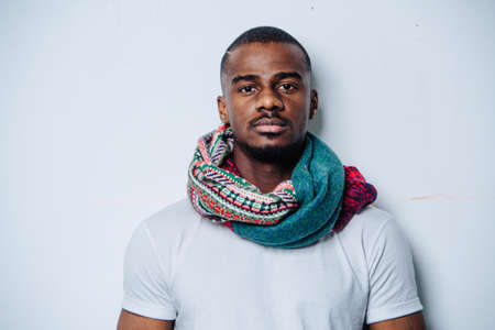 Head and shoulders portrait of an african american man over white wall. He is wearing white shirt and a colorful patterned scarf.の写真素材