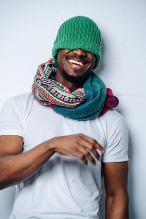 Laughing silly african american with a green winter hat pulled over his face. He is also wearing a colorful patterned scarf.の写真素材