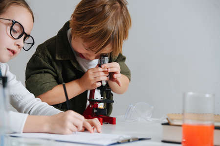Cringe little boy looking through the microscope, girl taking notes next to himの写真素材