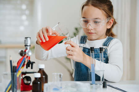 Calm little girl doing home science project, pouring red liquid into a flaskの写真素材