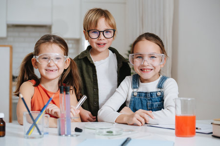 Portrait of three happy little kids doing home science project, all behid table.の写真素材