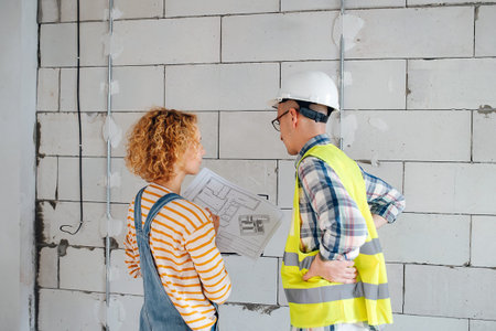 Behind view of an engineering team going over a blueprint, discussing it. Next to a brick wall...