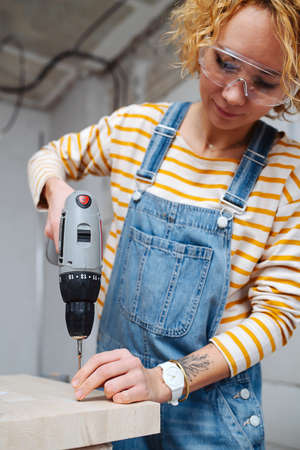 Focused female construction worker drilling a plank with an electric screwdriver. In a room inside a building under construction.の写真素材