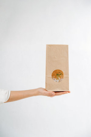 Open hand holding a paper bag with a green plant showing through a window in it.