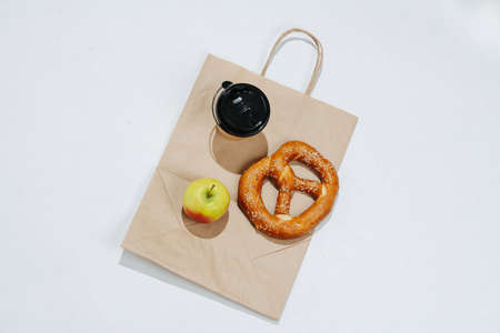 Top view composition of a cup of coffee, pretzel and an apple on a flat paper bag. Over white background.の写真素材