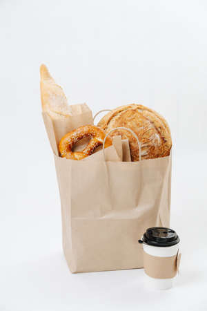 Golden pastry sticking out of a paper brown bag standing on the floor with coffee cup next to it. Over white background. Eco friendly compostable product.の写真素材
