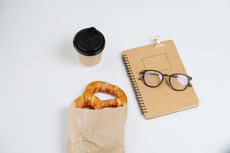 High angle composition of a cup of coffee, pastry and glasses on a notepad. Over white background.の写真素材