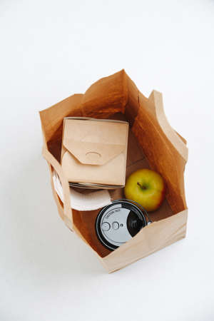 Overhead view of a lunch packed in a single use paper bag over white background. Apple, cup of coffee and a sealed paper box with a meal. Eco friendly packaging concept.の写真素材