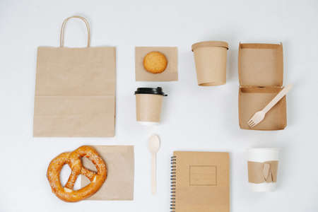 Paper eco friendly items arranged in composition. Carton compostable products over white. Cups, box, bag, cutlery, notepad completed with some pastry.の写真素材