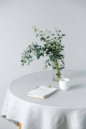 Folded paper sheet on a round table with a rough tablecloth and branch in a jar
