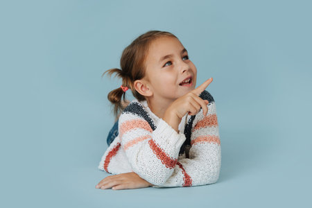 Social little girl in striped sweater lying on the floor over blue background. Talking to someone...