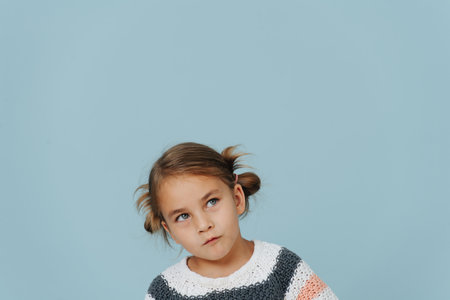 Looking up tight-lipped little girl in striped sweater, hair in buns over blue. A lot of copy space around.の写真素材